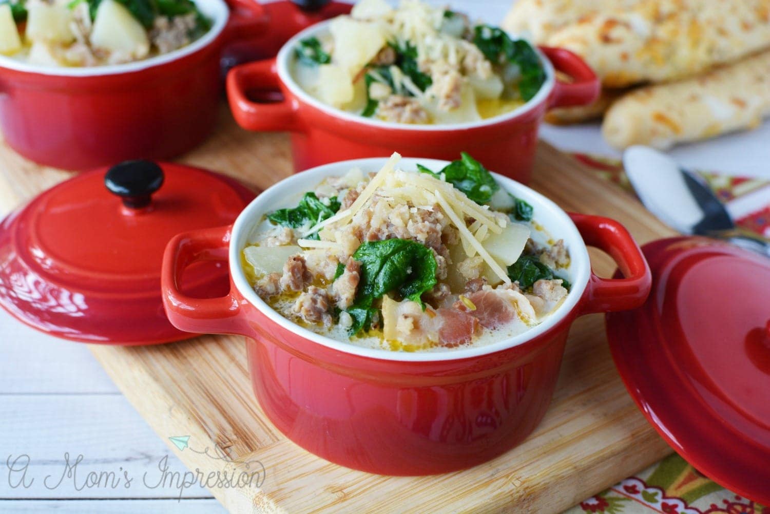 a bowl of pressure cooker zuppa toscana soup in a red crock on top of a cutting board 