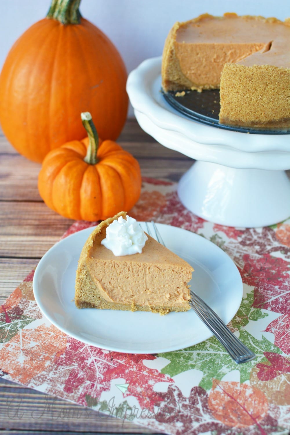 Instant Pot Pumpkin Cheesecake Recipe sitting on a table with two pumpkins.