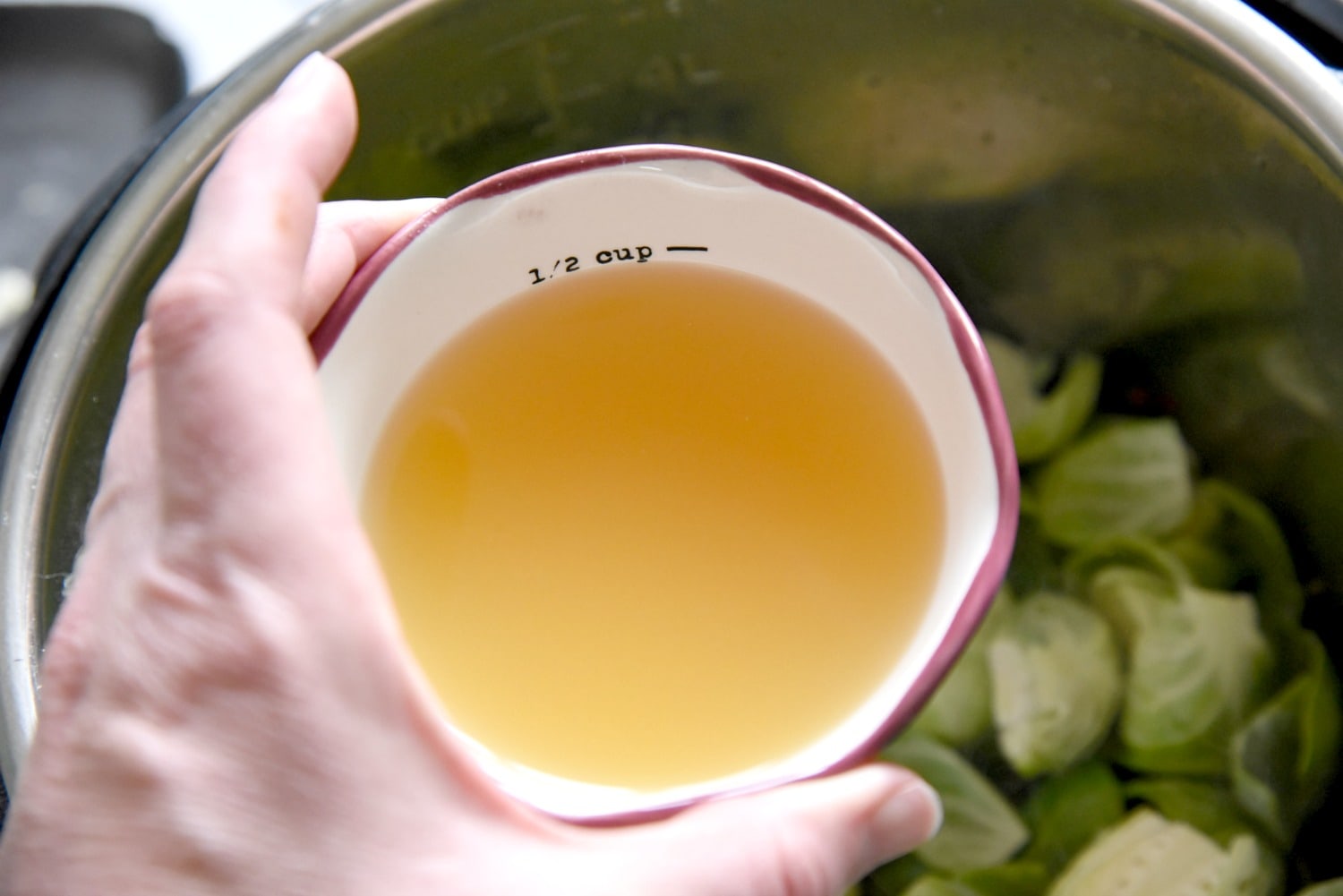 pouring chicken stock in the pressure cooker to cook brussels sprouts
