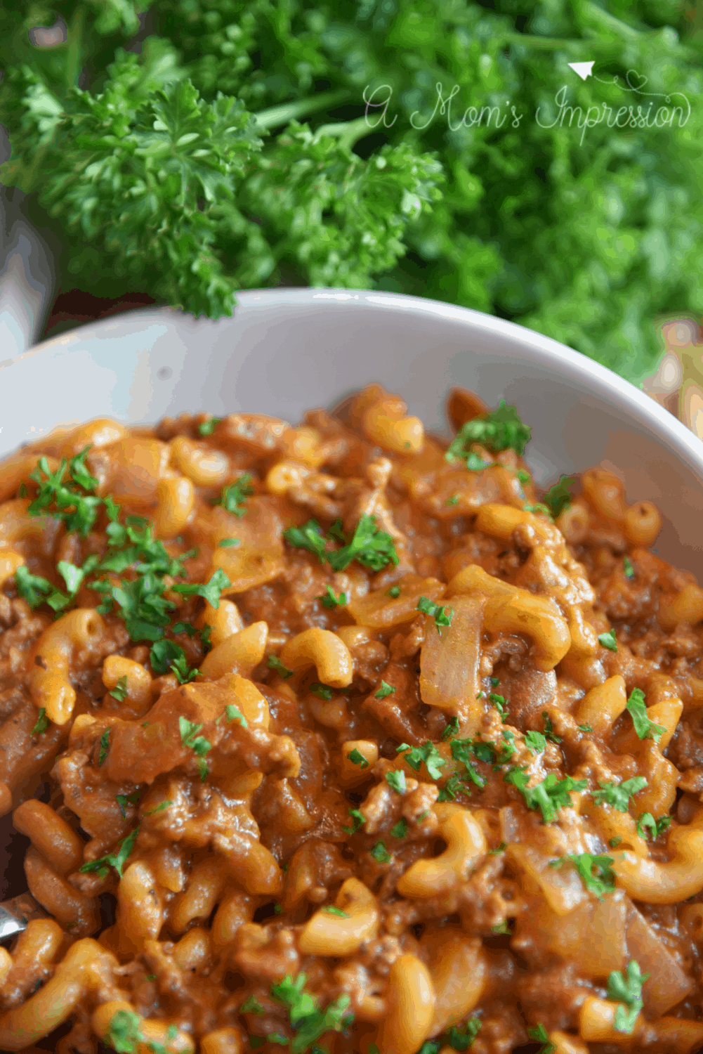 Old Fashioned Goulash Recipe in a bowl sitting on a table next to parsley. 