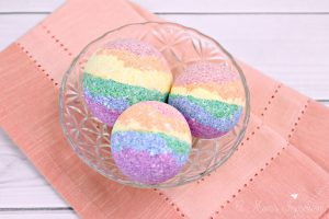 Three DIY rainbow bath bombs sitting in a bowl on a table