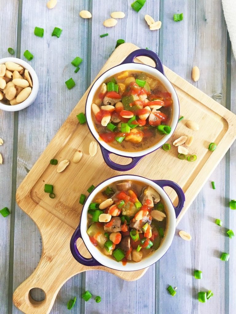 two bowls of Thai-peanut-chickpea-soup sitting on a cutting board 