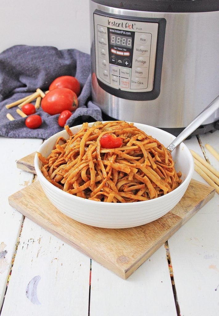 a bowl of instant-pot-pasta sitting on a cutting board in front of a pressure cooker