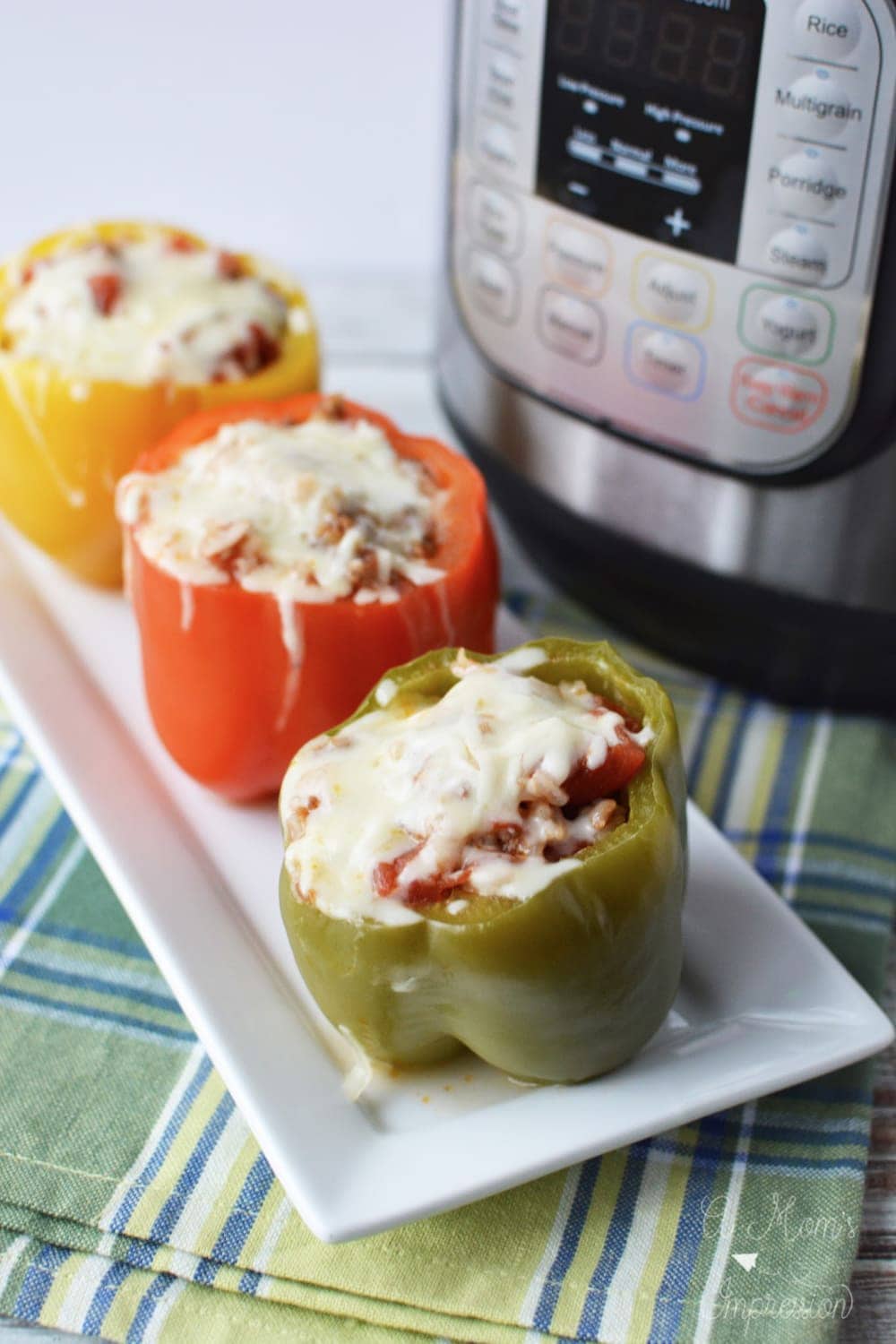 Instant Pot Sausage stuffed peppers on a white plate with a pressure cooker in the background