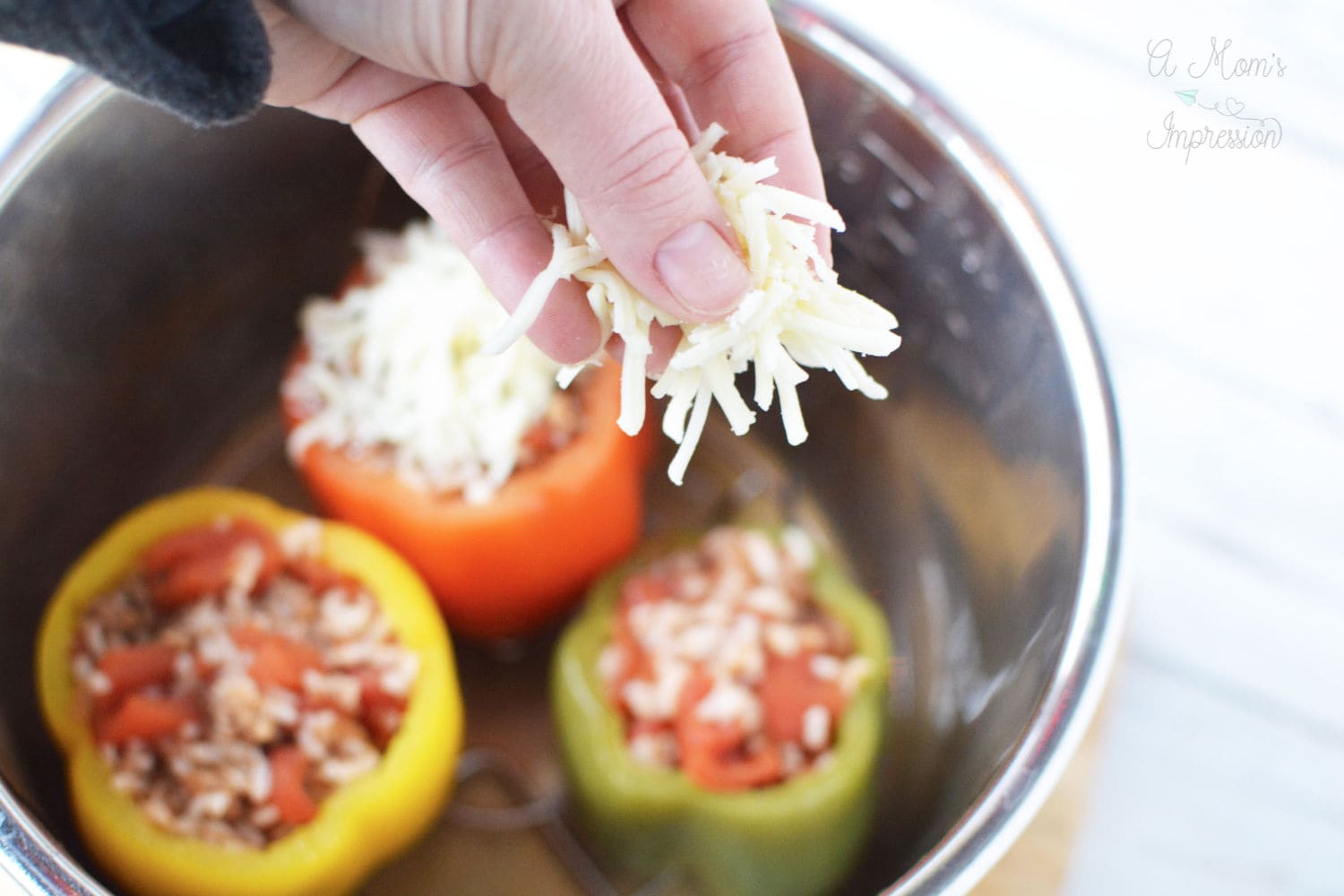 a hand with shredded cheese getting ready to put the cheese on top of a stuffed pepper