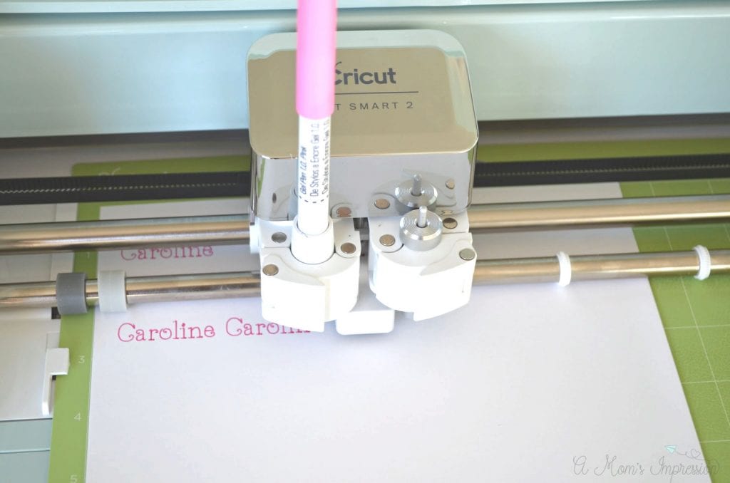 Cricut Explore Air 2 using a pink pen to draw a name