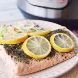 A plate with some salmon and lemon slices sitting in front of an Instant Pot pressure cooker