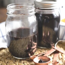 Two jars of homemade elderberry syrup in front of an Instant pot