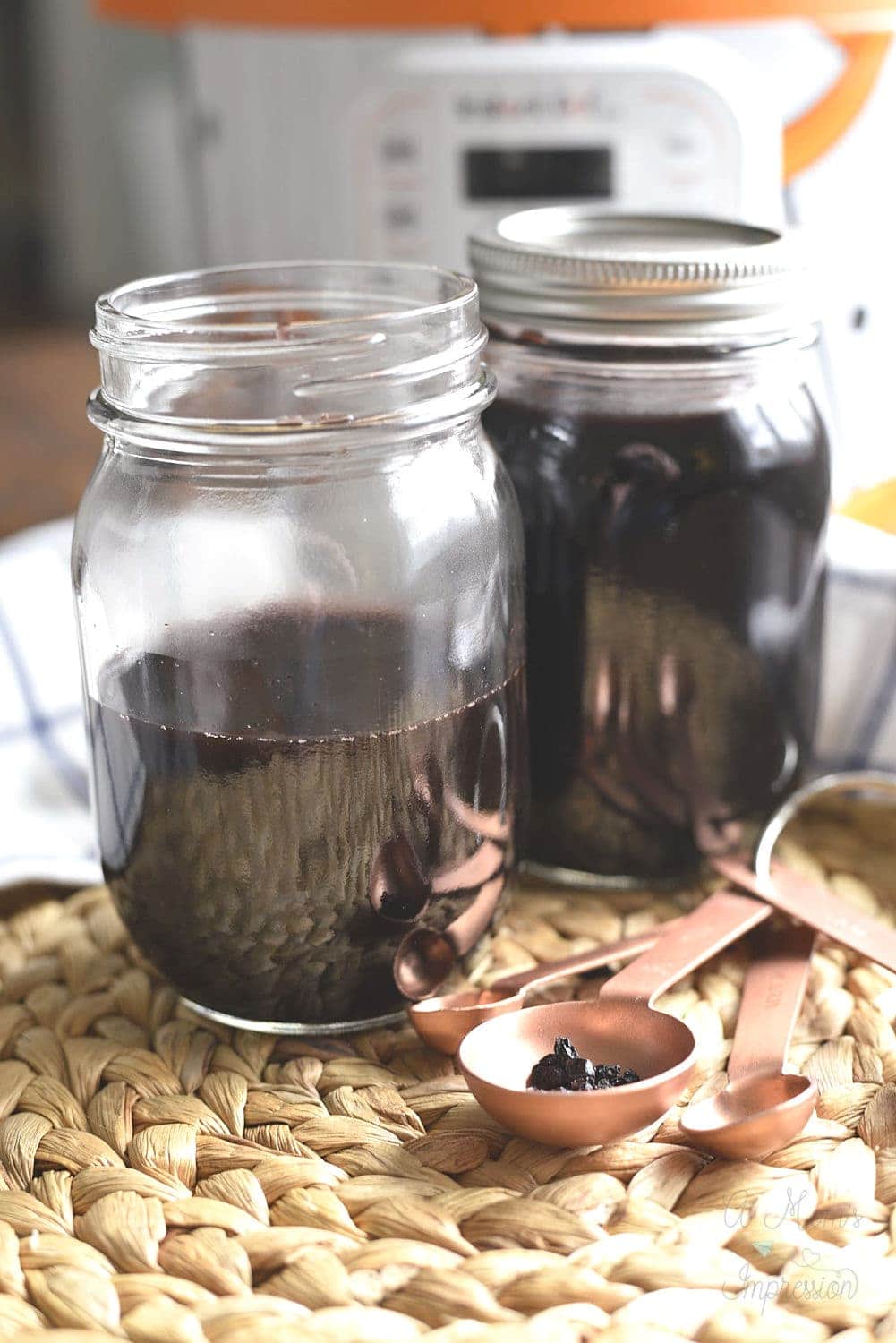 Two jars of homemade elderberry syrup in front of an Instant pot