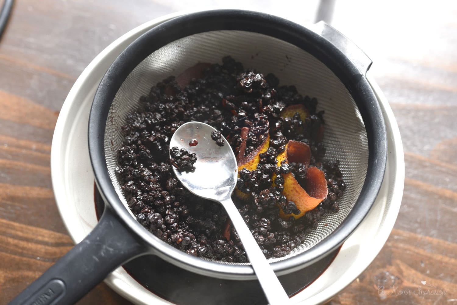 a bowl of cooked elderberries in a strainer over a bowl