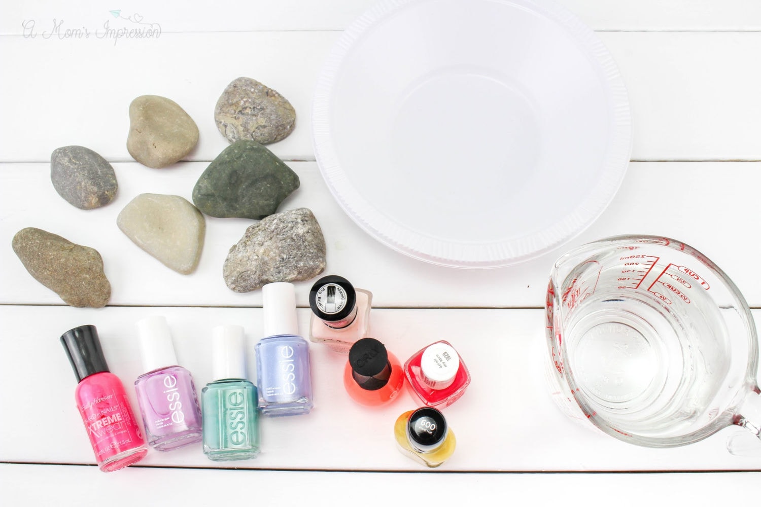 some rocks, nail polish, water and a bowl sitting on a white surface