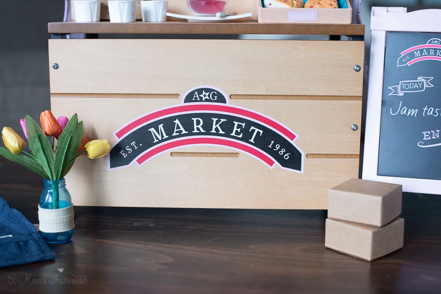 American Girl City Market stand with a small vase of flowers and cardboard boxes. 