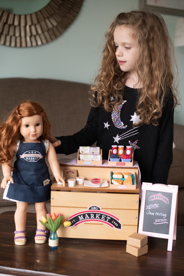 a girl playing with her doll in front of a market stand