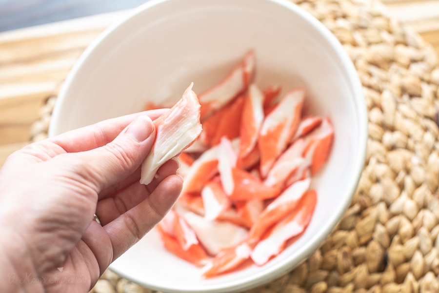 A personal holding a piece of Surimi Flakes in front of a bowl of Surimi Flakes 