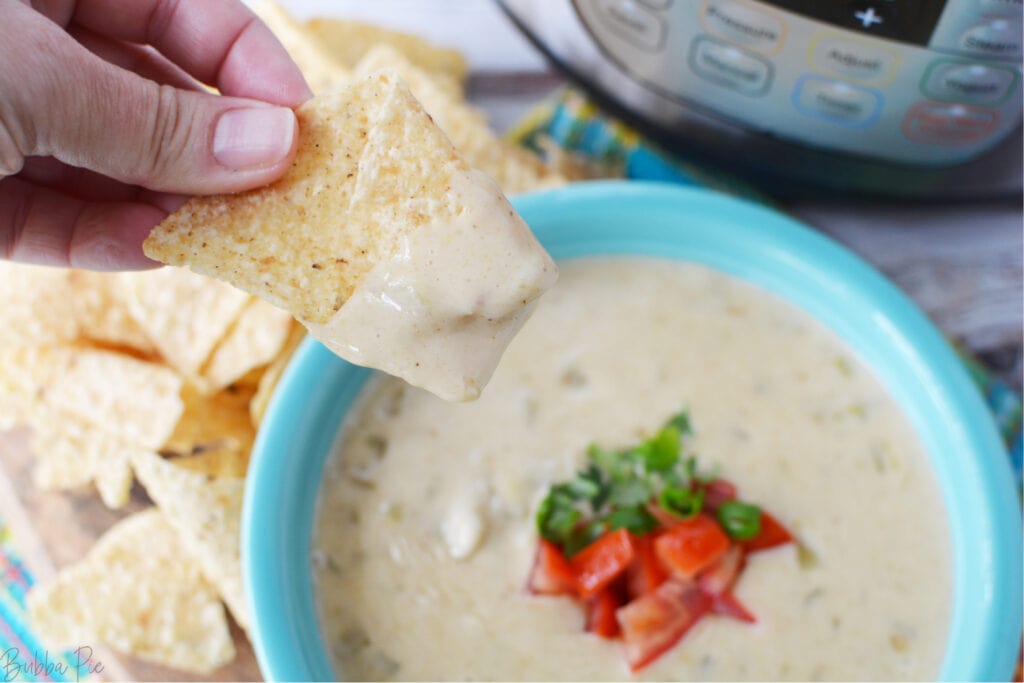 A chip being dipped into Pressure Cooker Queso dip.