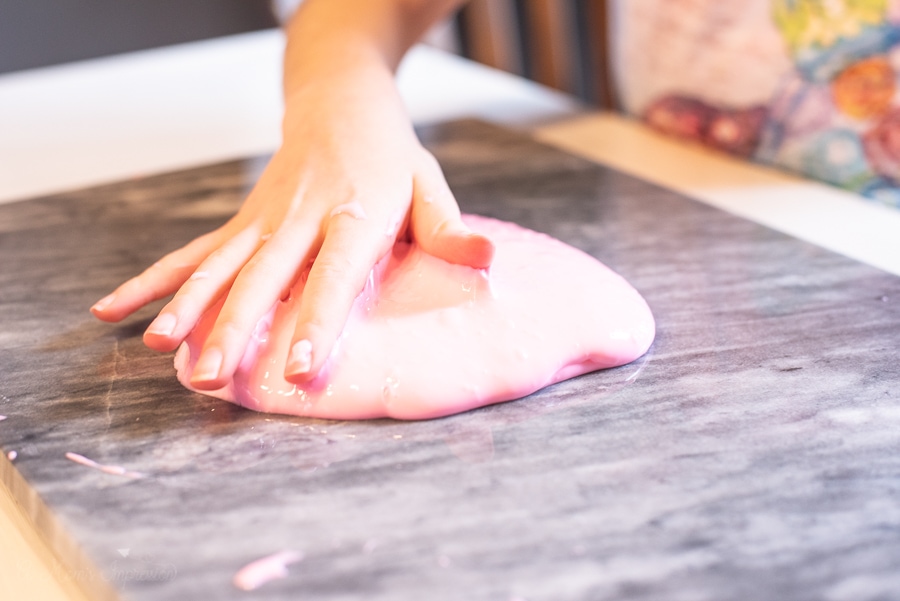 a kid's hand rolling out pink slime