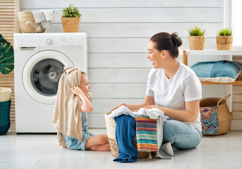 Beautiful young woman and child girl little helper are having fun and smiling while doing laundry at home.