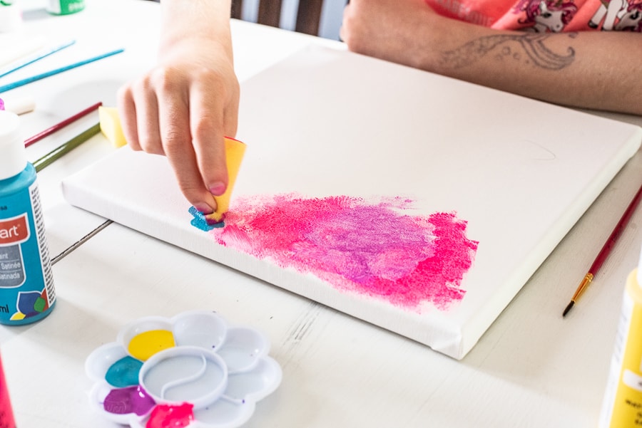 a girl using a foam brush to pain bright pink paint on a canvas