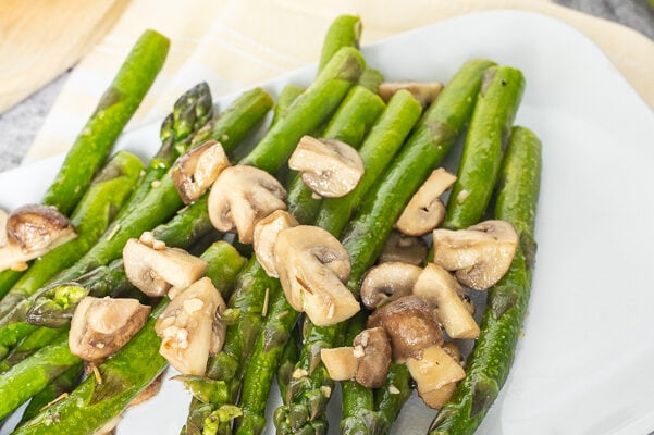 a white platter with asparagus with mushrooms