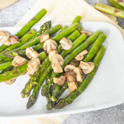 A side of asparagus with mushrooms on a white plate