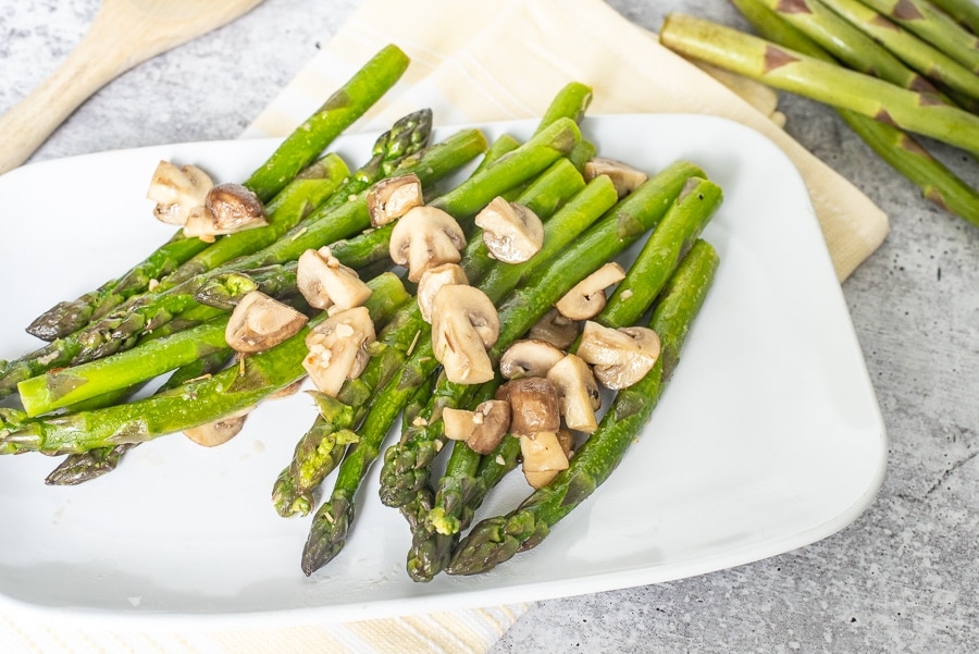 A side of asparagus with mushrooms on a white plate