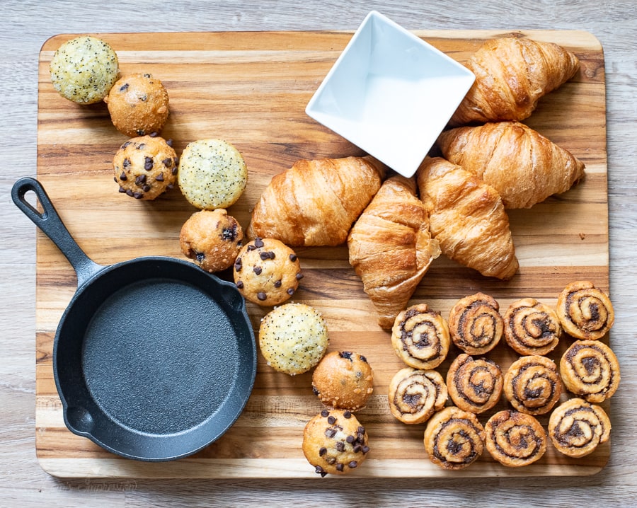 muffins, cinnamon rolls, and croissants on a cutting board